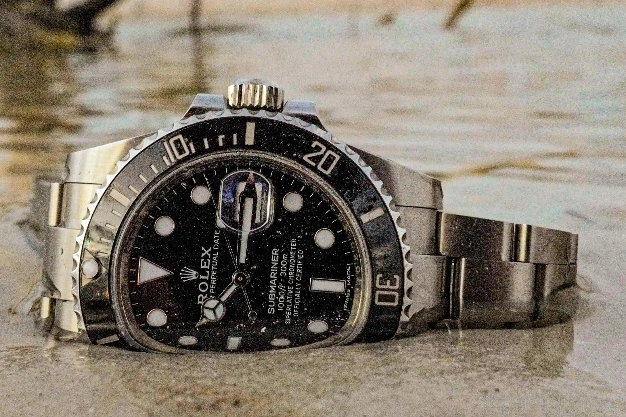 Rolex watch with a metallic band on a a beach in the water on the sand