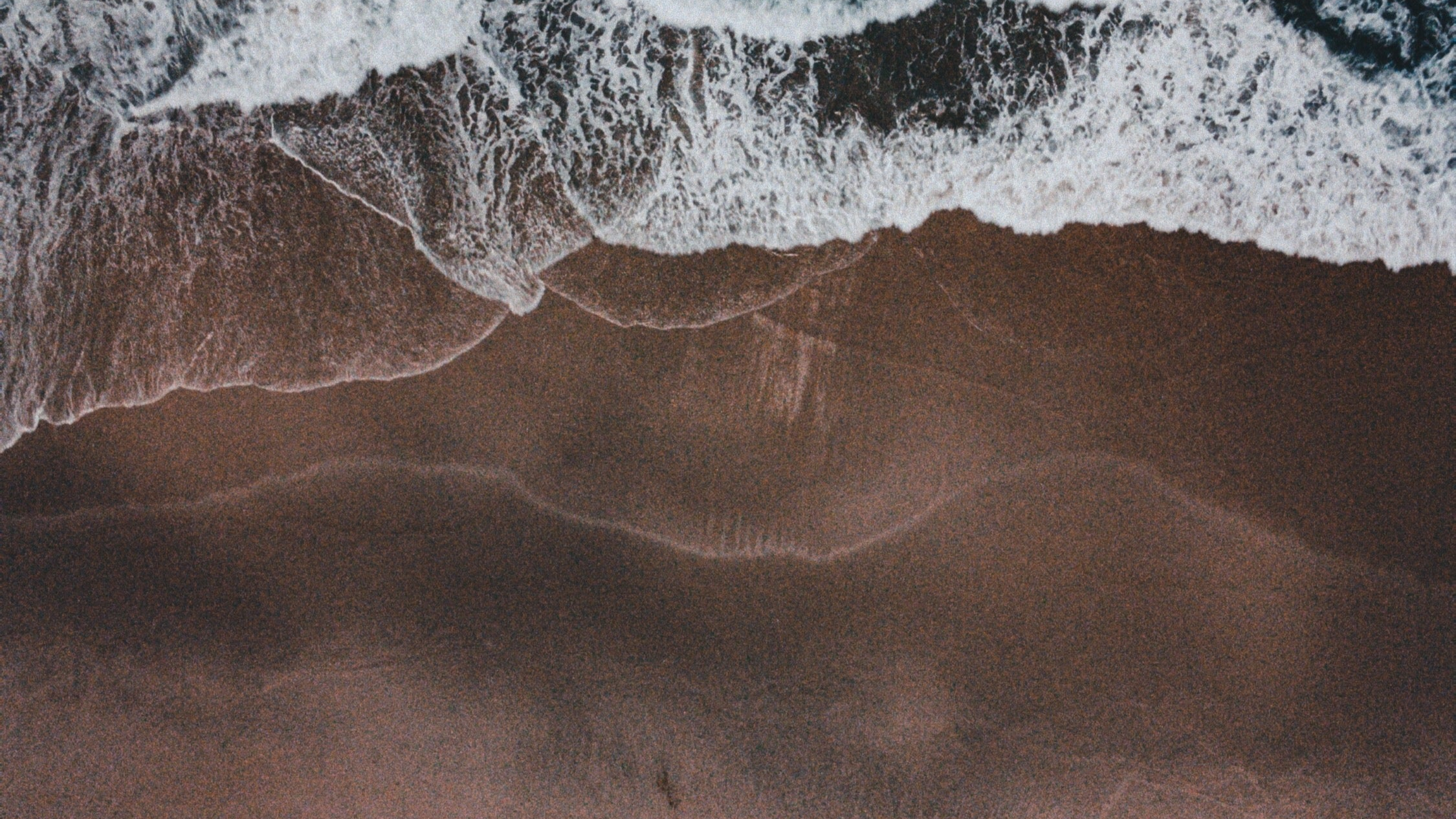 Top-down view of waves crashing onto a sandy beach